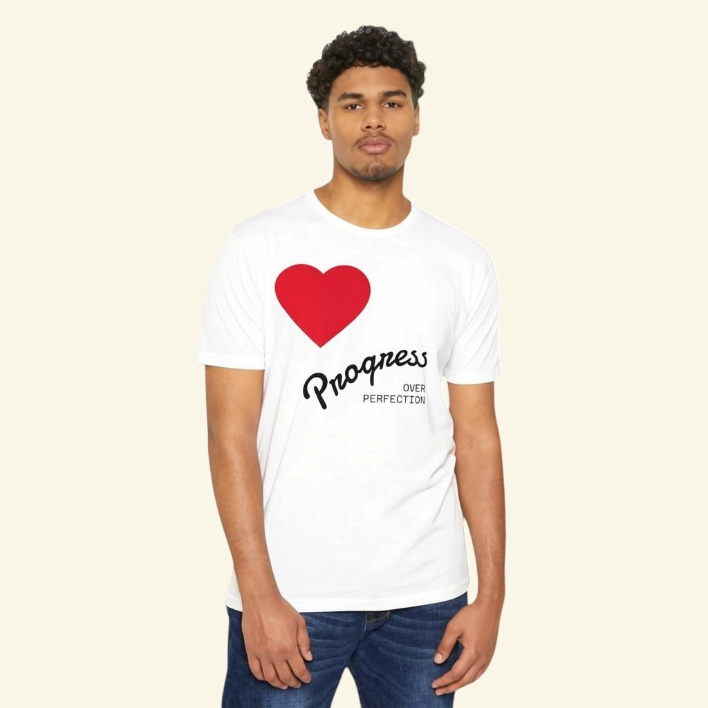 A man wearing a white PURETE cotton blend t-shirt featuring a red heart and Progress Over Perfection text graphic.