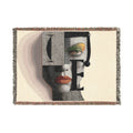 PURETE woven cotton throw blanket featuring a bold abstract portrait with geometric shapes and fringed edges.
