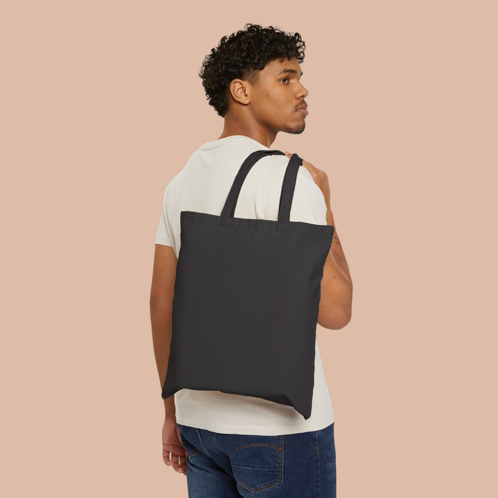 A man wearing a plain black PURETE cotton canvas tote bag over his shoulder against a white background.