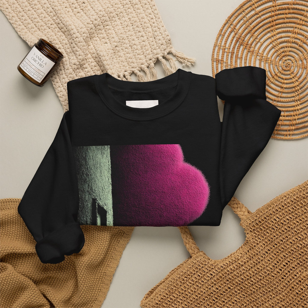 PURETE black crewneck sweatshirt with a pink heart graphic, laid flat with a candle and woven accessories.
