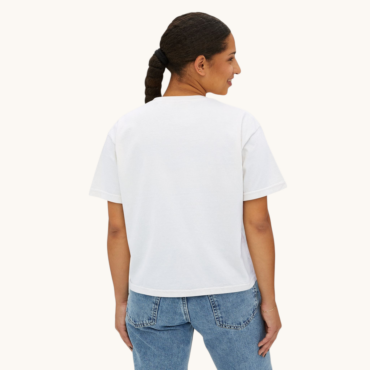 A woman wearing a white PURETE oversized boxy cotton t-shirt, viewed from the back, paired with blue denim jeans.